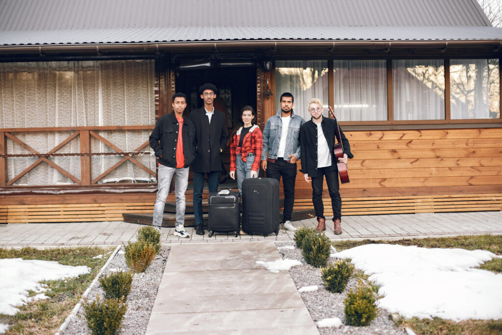 Group frinends with suitcases standing at wooden building
